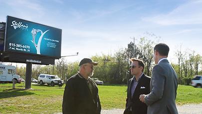 Customers speak with Watchfire territory managers at the base of a billboard structure.